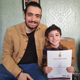 Alberto with his son holding his Trinity graded exam certificate