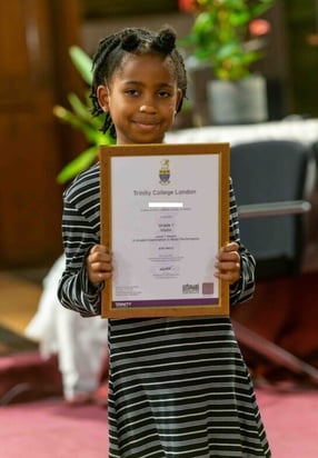 Young girl holds up her framed Trinity exam certificate