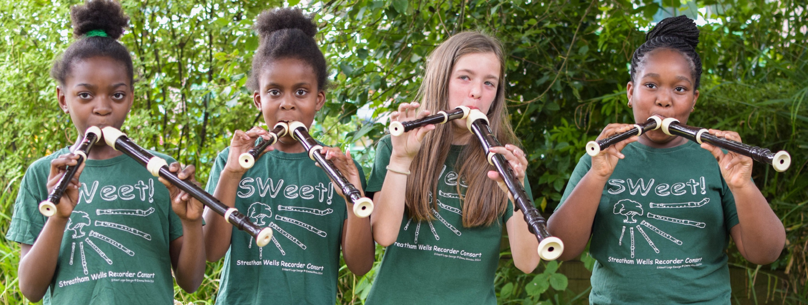 Three black and one white girl standing in a line wearing SWeet! Recorders Consort CIC t-shirts. Each of them appears to be playing two recorders at the same time.