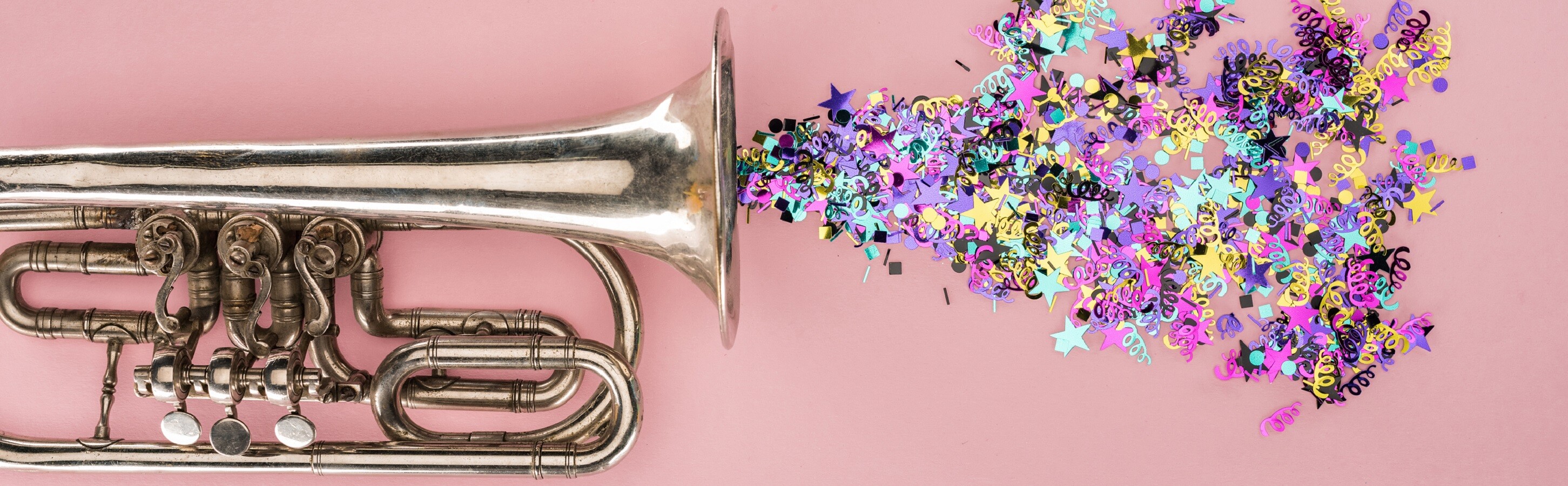 Brass instrument on pink background with confetti blasting out of the bell