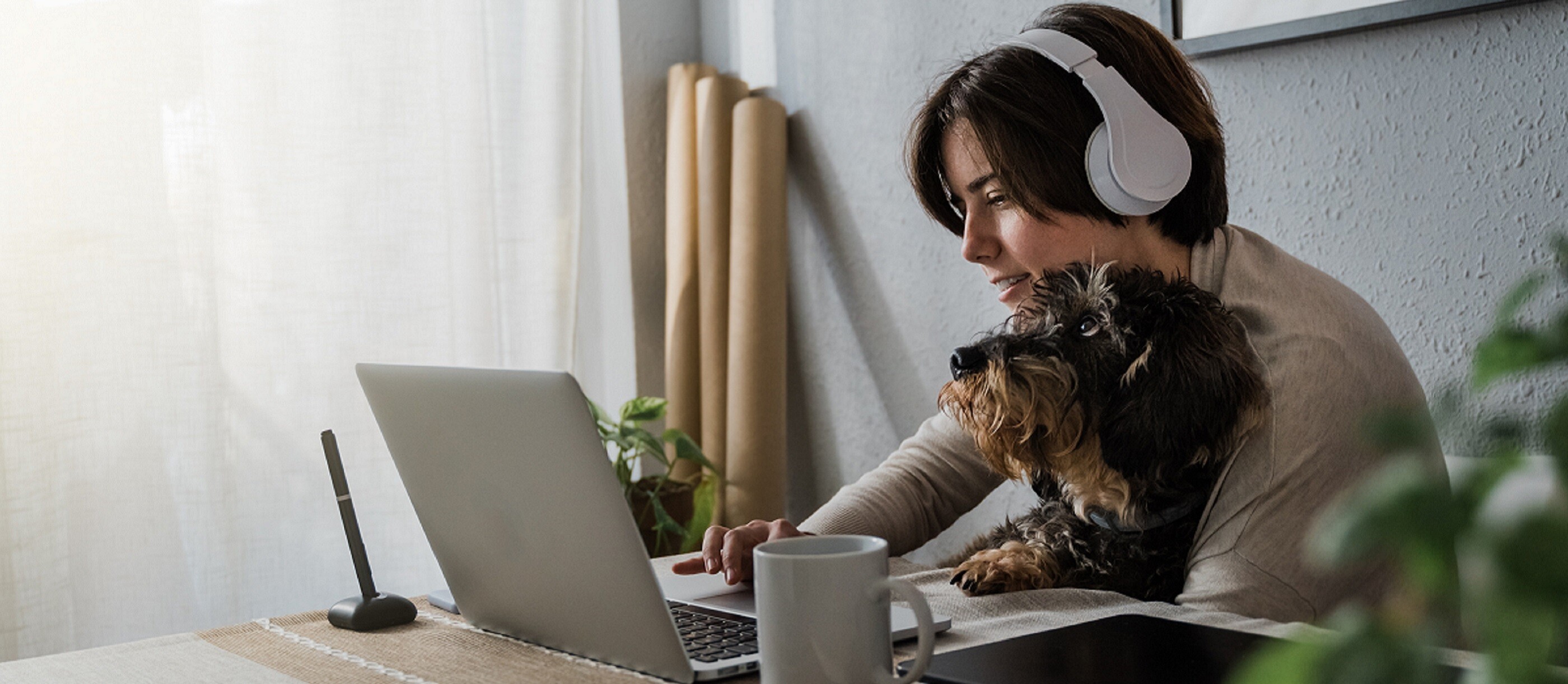 Woman wearing headphones with dog on lap working at a laptop