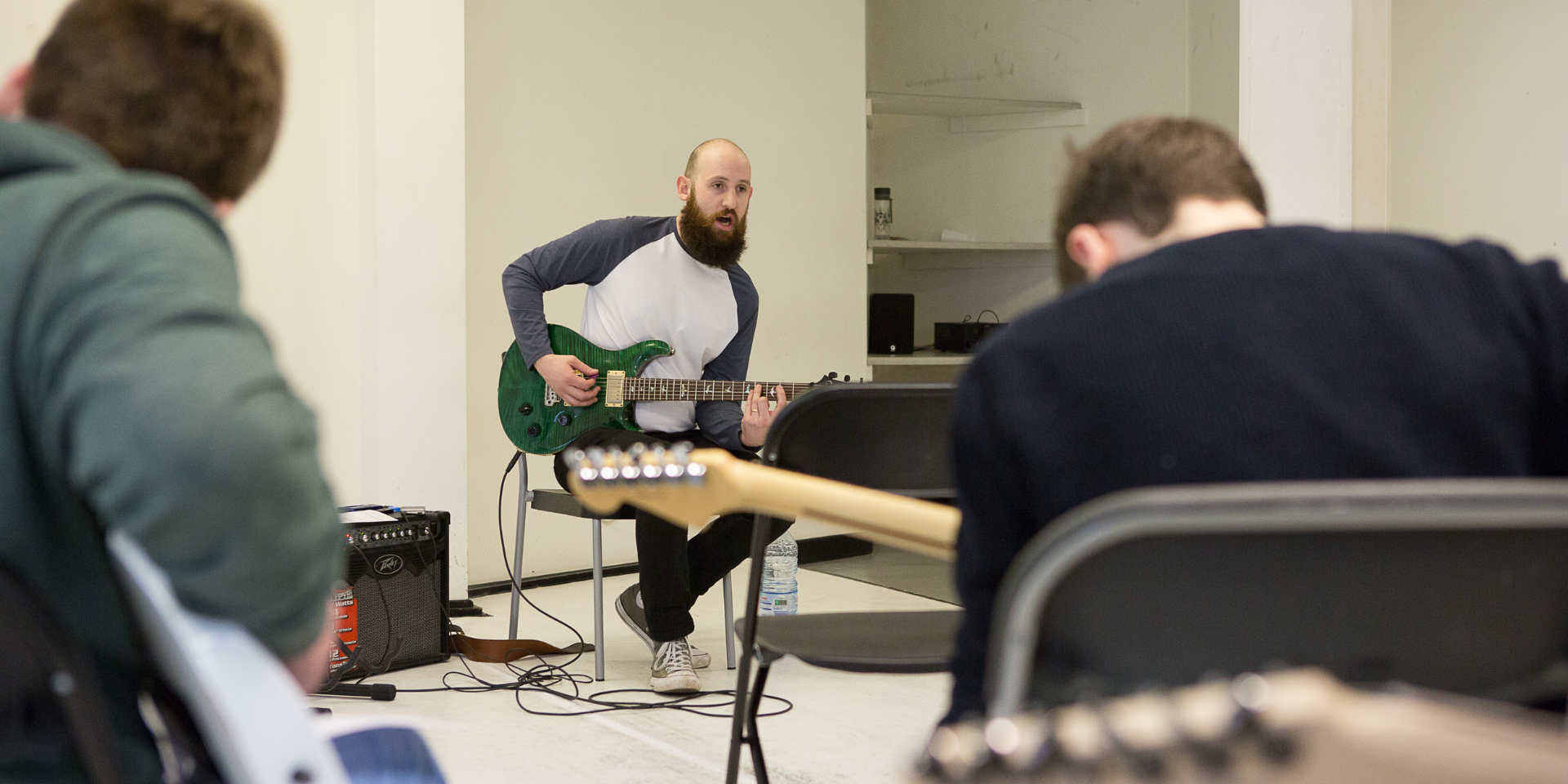 Male teacher playing electric guitar in front of students