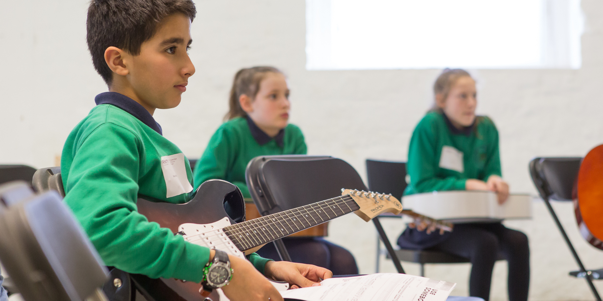 Young boy with electric guitar and two young girls in a clasroom 