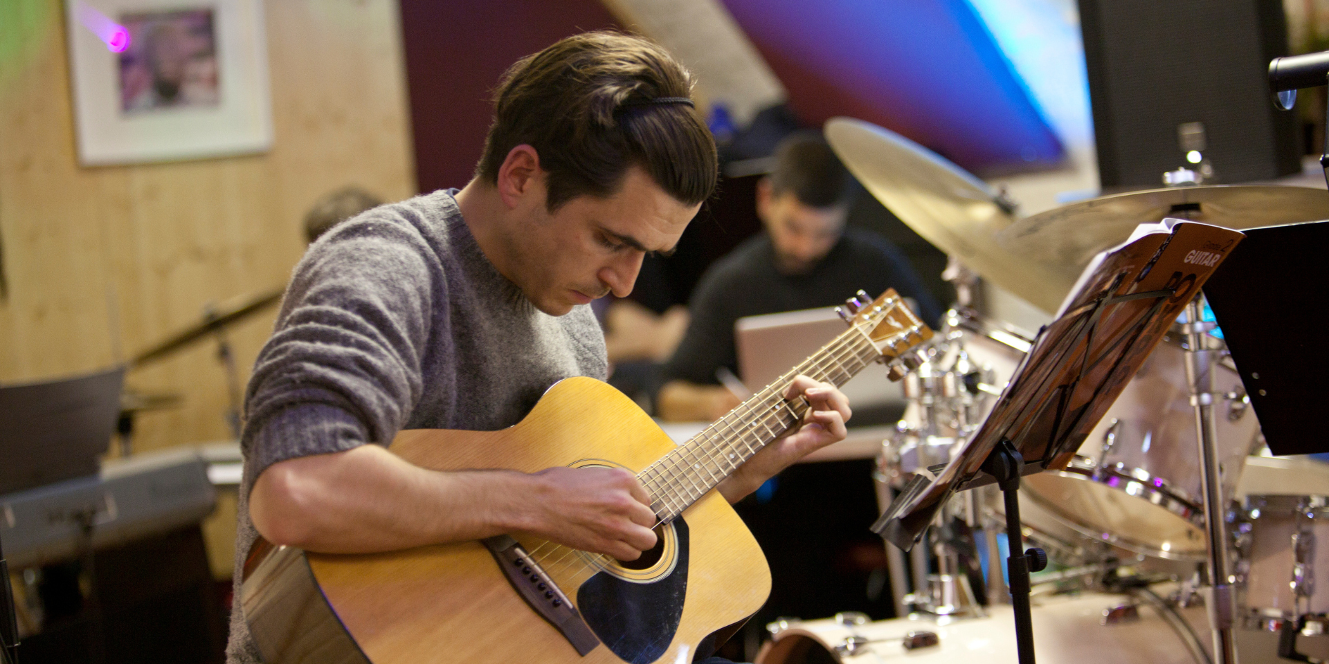 White male playing an acoustic guitar with examiner in background