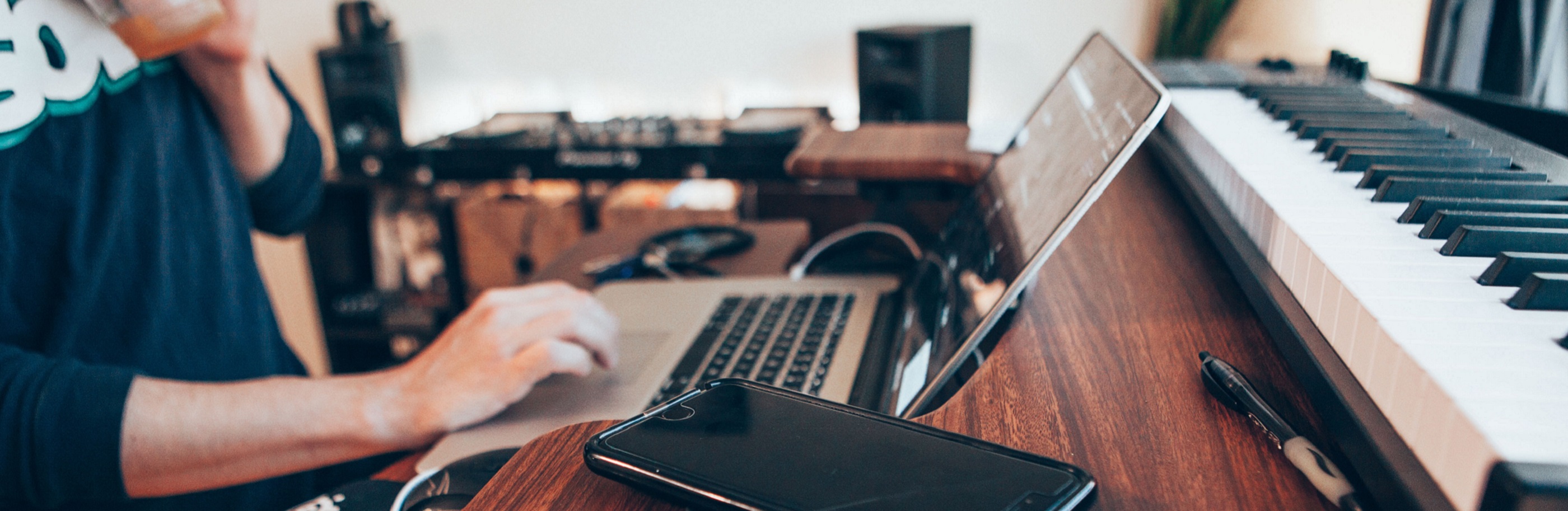 Man sat at a laptop with smartphone to their side and keyboard behind the computer