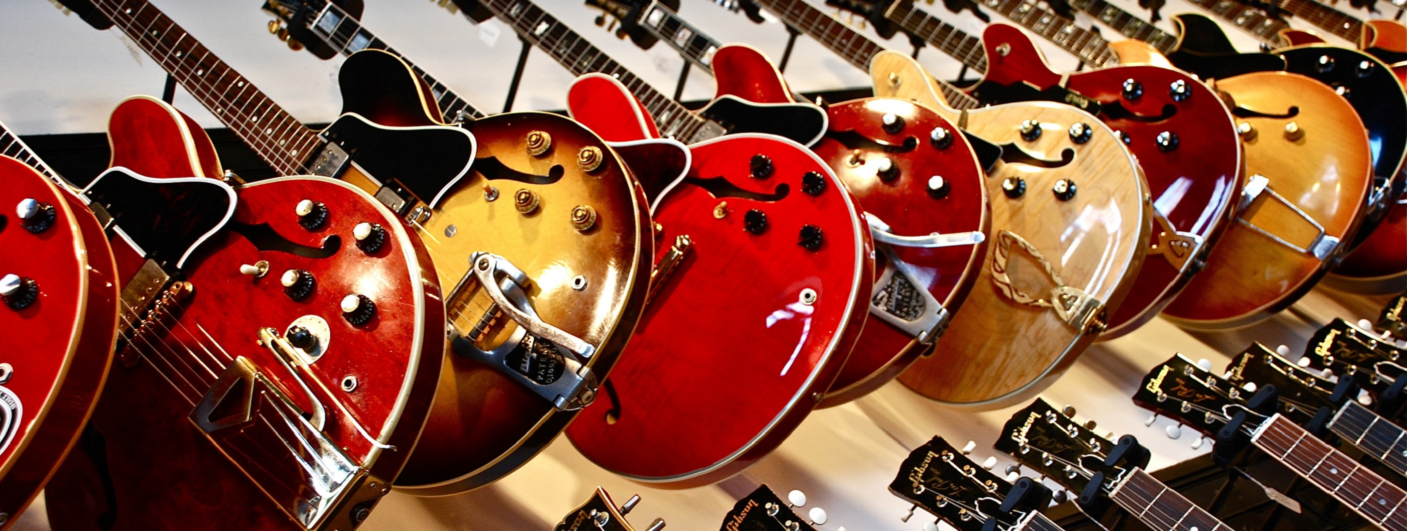 Red and gold coloured Gibson guitars hanging in a row on a wall